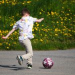 a young boy kicking a soccer ball on a road